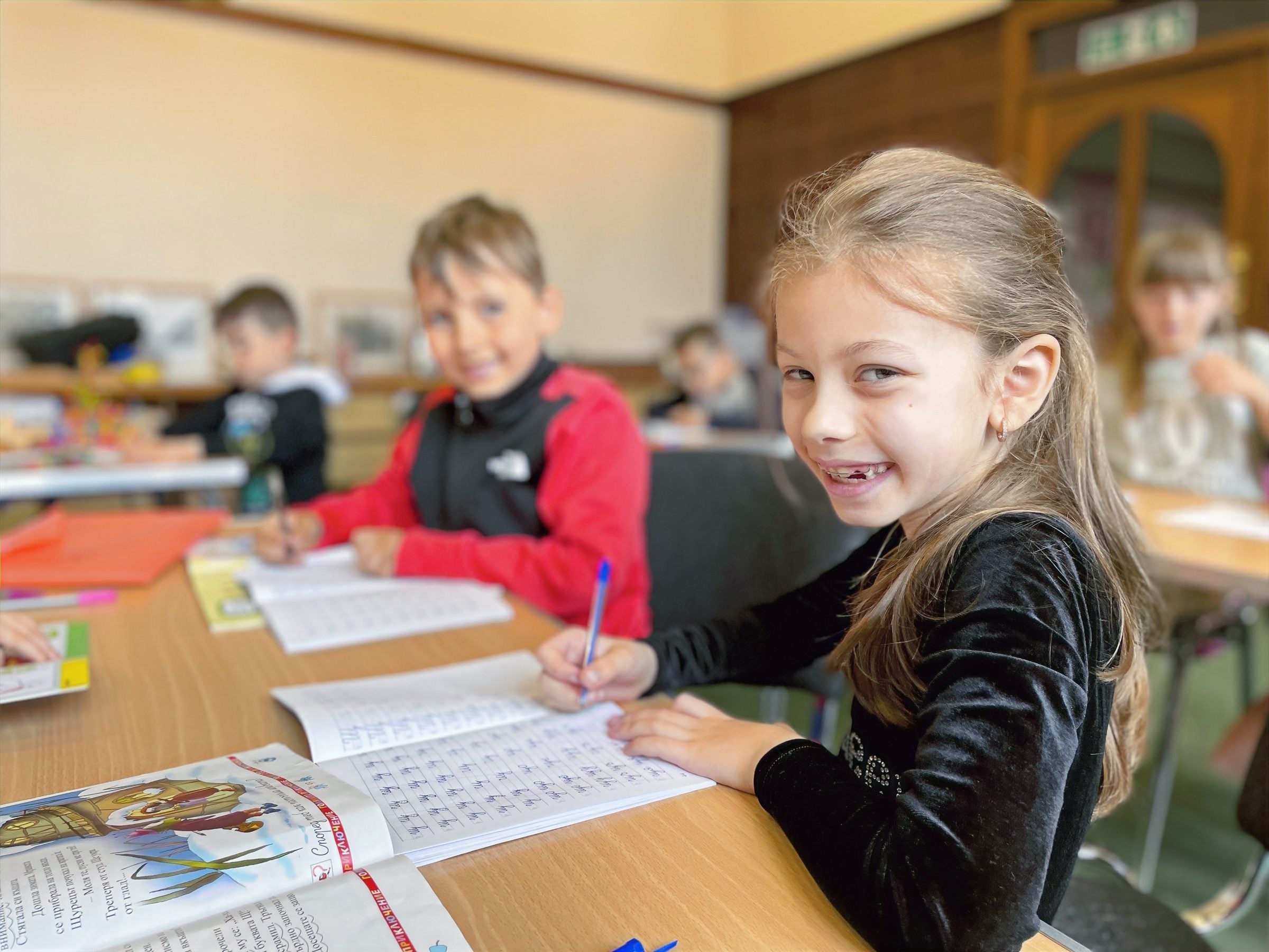 A smiling girl writing in her Bulgarian workbook at Azbukarche school